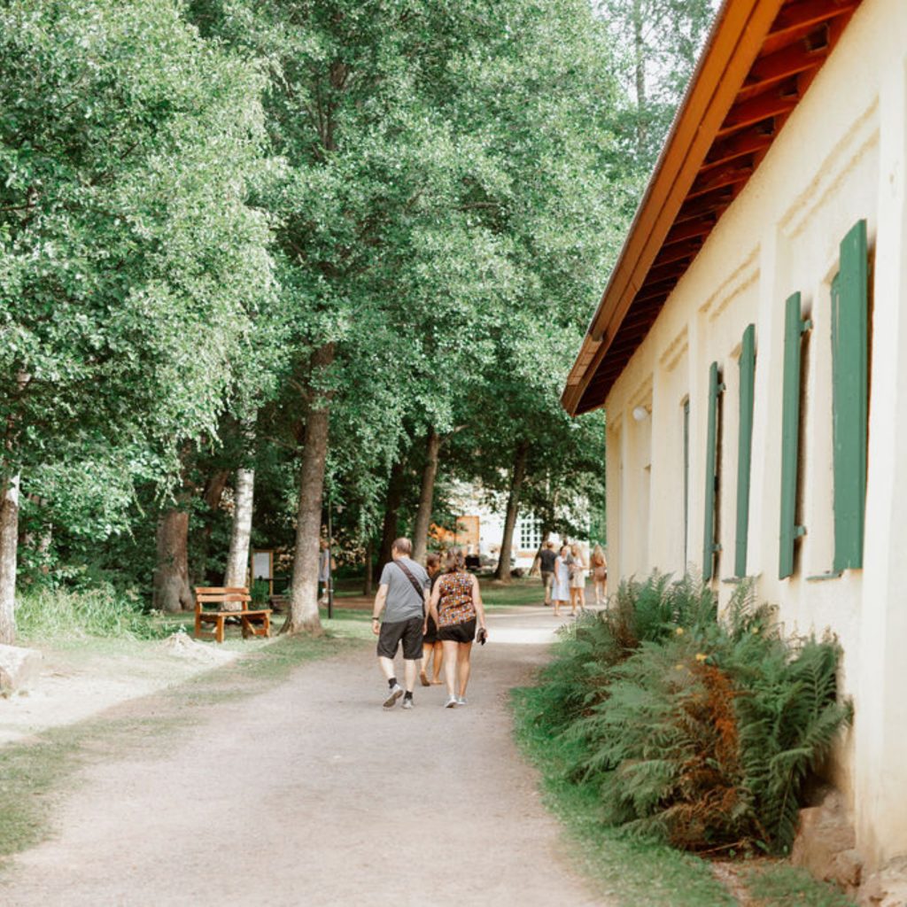 Pariskunta kävelee vehreänä kesäpäivänä Mathildedalin Ruukilla. Kuvassa oikeassa laidassa historiallinen keltaisen värinen kankirautavarasto.